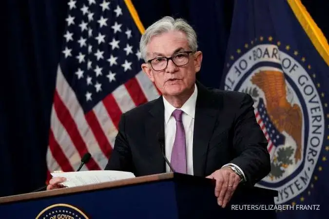 Federal Reserve Chair delivering a speech at a press conference, holding documents