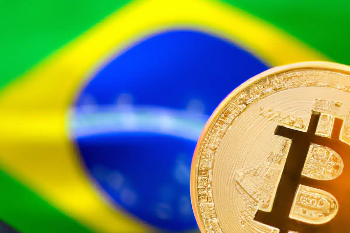 Foco no Bitcoin em frente à bandeira brasileira, representando a adoção de criptomoedas e a regulamentação da moeda digital no Brasil