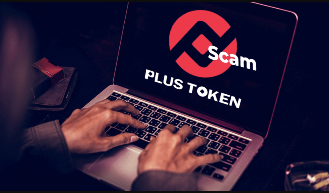 Close-up of hands typing on a laptop displaying the PlusToken logo labeled with the word “Scam”, highlighting one of the largest cryptocurrency Ponzi schemes.