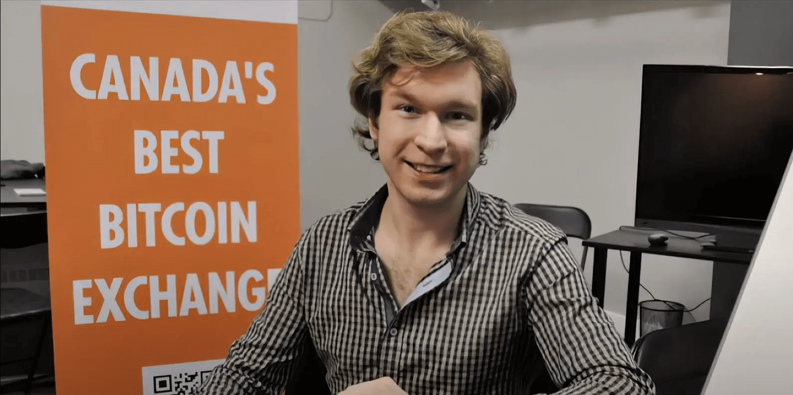 Gerald Cotten, founder of Canadian crypto exchange QuadrigaCX, smiling at a desk with a banner reading “Canada’s Best Bitcoin Exchange” in the background, later revealed to be at the center of a major cryptocurrency scandal.