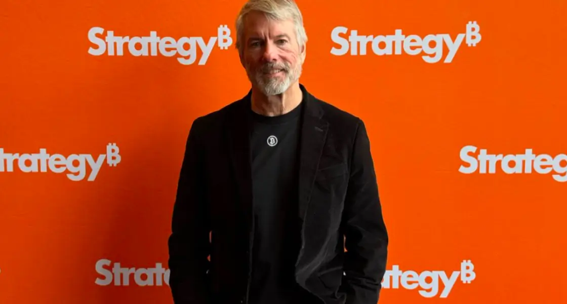 Man in front of Strategy₿ panel with Bitcoin logo on his t-shirt, indicating company event or promotional action.
