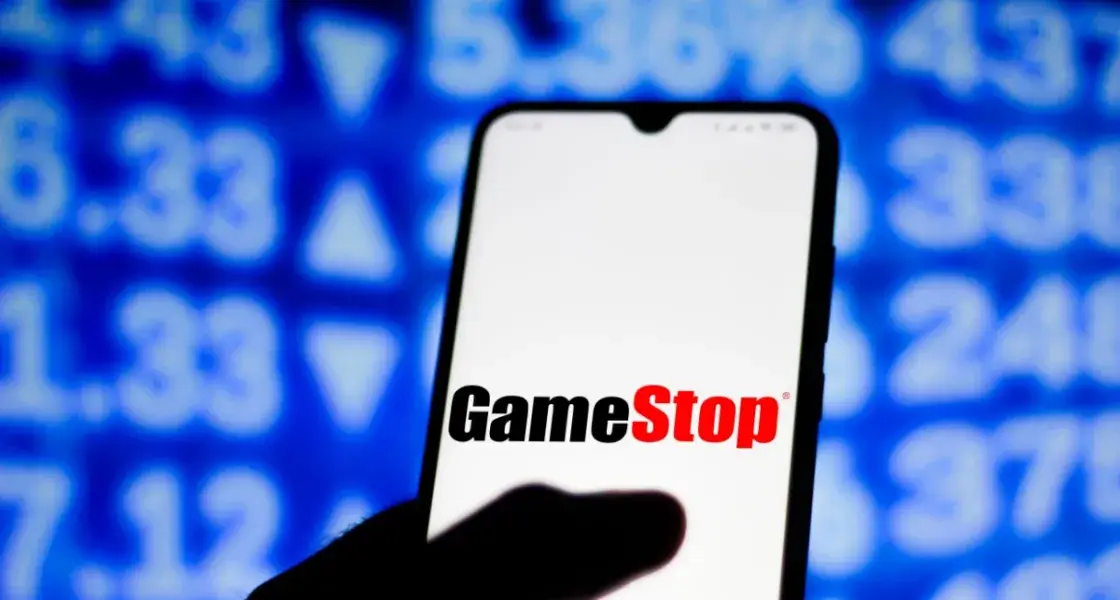 GameStop logo on cell phone with stock numbers background, suggesting market analysis or investment in the company.